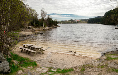 Fototapeta na wymiar A picnic table with benches on a small sand beach of Eivindsvannet lake in Djupadalen public recreational area, Haugesund, Norway, May 2018