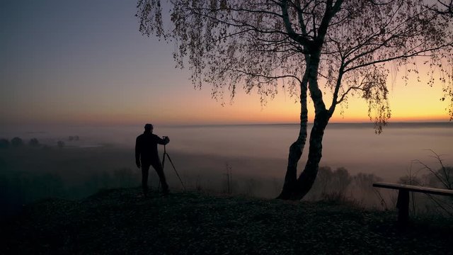 photographer takes pictures of morning fog over the river, man take pictures on dawn over the river in the morning mist, Sunny and foggy morning over the river, Photographer taking photo at dawn