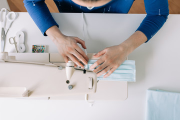 Woman hands using the sewing machine to sew the face home made diy medical mask during the coronavirus pandemia.