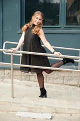 Photo of a fashionable blonde girl in a dress on the background of the steps of a building outdoors in the spring city