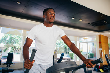 Side view of fit African American man in sportswear doing steps on elliptical machine during...