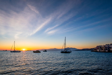 Sunset in Mykonos island, Greece with yachts in the harbor and colorful waterfront houses of Little...