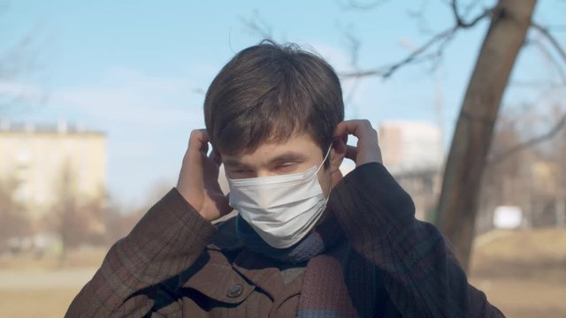 Close up portrait of a young handsome man putting on a protective mask outdoors in the city. Sunny sping day. Protect yourself and your loved ones. Covid-19 pandemic