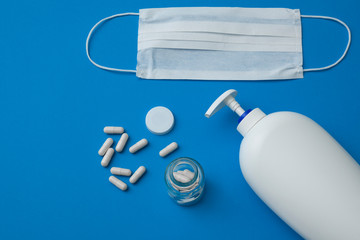 facial disposable medical mask, white pills and liquid hand soap isolated on blue background.