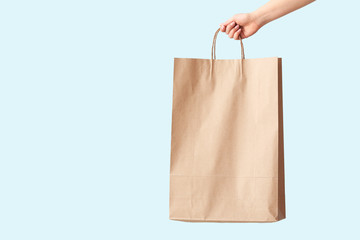 Female hand with paper shopping bag on color background