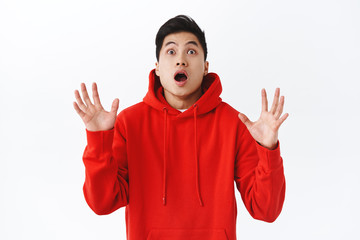Waist-up portrait of shocked, startled asian man raise hands to catch something falling from sky, gasping and look alarmed or focused, see object flying into his arms, white background
