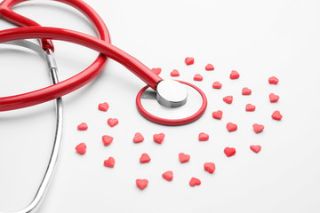 Stethoscope and heart-shaped pills on white background