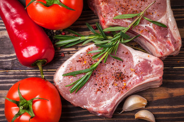  Pork steak with spices, vegetables and rosemary. Juicy and fresh raw meat, tomatoes, paprika, henna, and peppercorns on a wooden tabletop
