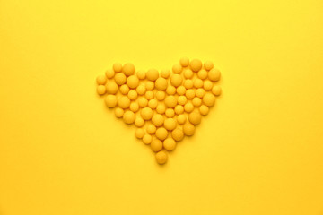 Heart made of pills on color background