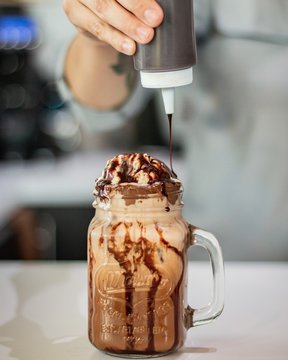 Closeup shot of a person adding chocolate syrup on a milkshake in a mason jar