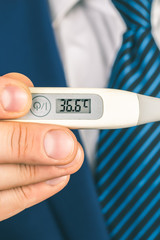 A man in a suit and tie holds in his hands an electronic thermometer with temperature