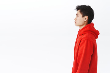 Profile portrait of young asian man in red hoodie looking left with serious, unbothered expression,...