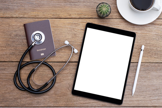 Travel insurance concept. Mockup image of digital tablet with blank white screen, passport, medical stethoscope and cup of coffee. Top view.