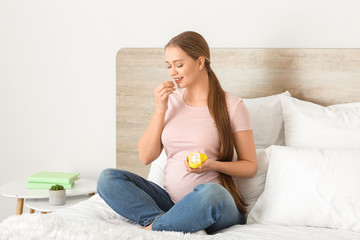 Young pregnant woman taking pill at home