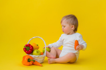 baby in a white bodysuit with vegetables, sitting on a yellow background. healthy food for the child, space for text