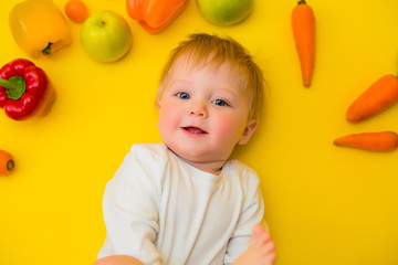 Fototapeta na wymiar Healthy child nutrition, food background, top view. Smiling baby 8 months old surrounded with different fresh fruits and vegetables on yellow background. Baby first solid feeding.baby with vegetables