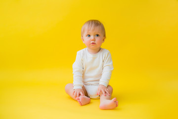 Naklejka premium Healthy baby in white bodysuit sits on a yellow background, space for text