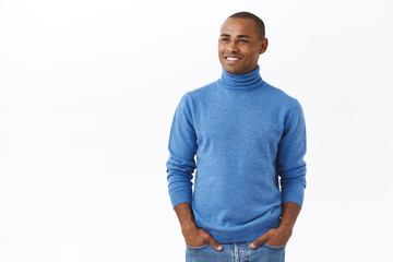 Business, investmenent and profit concept. Portrait of pleased, happy young elegant african-american male entrepreneur in blue turtleneck, hold hands in pockets, looking left with satisfied smile