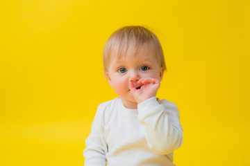 Healthy baby in white bodysuit sits on a yellow background, space for text