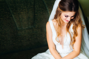 Fototapeta premium bride sits on sofa in wedding dress with wedding veil and smiles