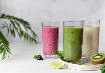 Colorful smoothie drinks with ingredients (kiwi, banana, blackberry). Natural Organic Food Style. gray background with green leaves. horizontal image, selective focus.