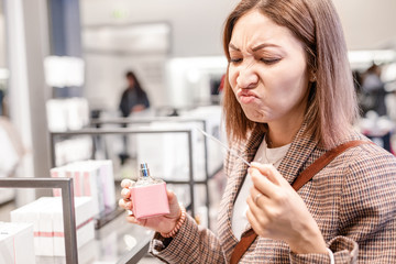 Asian woman sniffs perfume with a disgusting and terrible fragrance. Concept of bad taste and loss of smell