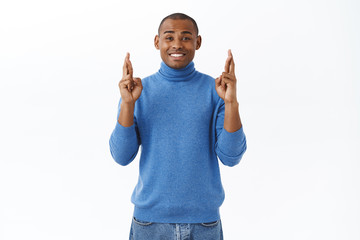 Portrait of optimistic, hopeful african-american man cross fingers for good luck, anticipating...