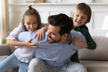 Playful young daddy having fun with energetic little daughter and son on sofa. Happy bearded father...