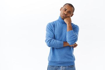 Portrait of bored, reluctant young african-american man looking unimpressed at camera, lean head on fist and watching something with boring expression, homesick over white background