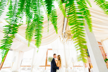 fern leaves in the foreground. profile of newlyweds in each othe