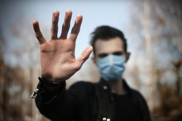 Young man wearing a medical protective mask against the Coronavirus Covid 19, showing stop hands gesture to stop the infectious virus outbreak.