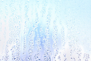 Moisture drops and water lanes on glass. Blue sky close up background