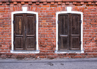 Vintage architecture red brick facade building two windows white stone frame, brown wooden shutters. Front view.