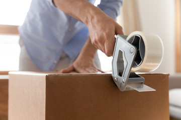 Close up young man using adhesive scotch, packing carton parcel box at home. Male removal service...