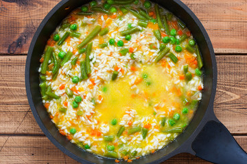 Step by step preparation of risotto with vegetables, step 5 - mixing fried vegetables, rice and broth, top view, selective focus