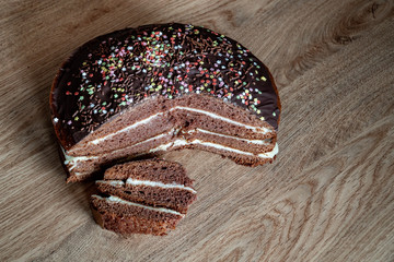 Delicious chocolate cake on plate on table on dark background. On a wooden stand with a slice of cut cake. Top view. Copy space