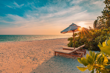 Beautiful tropical sunset scenery, two sun beds, loungers, umbrella under palm tree. White sand, sea view with horizon, colorful twilight sky, calmness and relaxation. Inspirational beach resort hotel