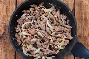 Step-by-step preparation of beef stroganoff, step 4 - connection of fried beef with fried onions, top view, selective focus