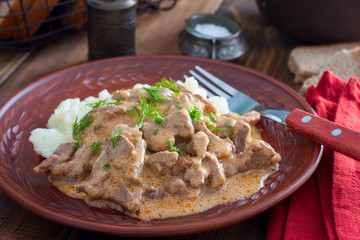 Traditional beef stroganoff in a ceramic bowl with mashed potato on a wooden table, selective focus