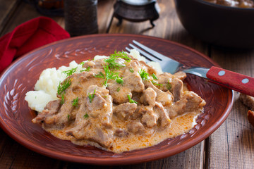 Traditional beef stroganoff in a ceramic bowl with mashed potato on a wooden table, selective focus