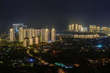 Obraz premium Night view of Sanya city with bright multi-colored illumination buildings, structures, roads, sidewalks, poles, bridges.