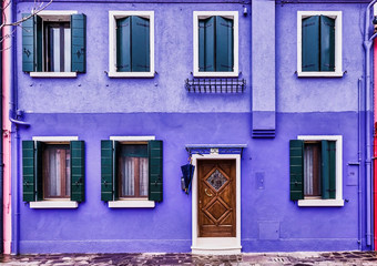Fototapeta na wymiar Facade of a violet house with small windows, located in Burano (Italy). Colorful house.