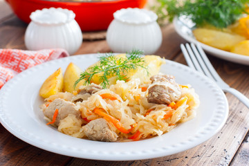 Sauerkraut stew with meat on a white plate with potatoes, selective focus