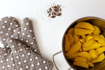 Flat lay - Potato sliced water-drenched in stainless steel pot, cotton gloves left with salt and cumin on white 