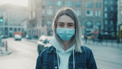 Young serously woman in medical mask standing in city street looking to camera road with cars on background Concept of health and safety life COVID-19 coronavirus virus protection pandemic in world - Powered by Adobe