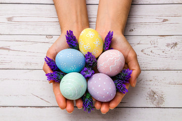 easter concept. closeup beautiful woman hands holding hand-painted easter eggs in tender pastel colors and lavender flowers over wooden table