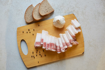 Flat lay of several pieces of bread, cutting board with salo, garlic and peppercorn, having eat break, being fond of Ukrainian dishes, time for tasty food, top view of Ukrainian traditional meal.