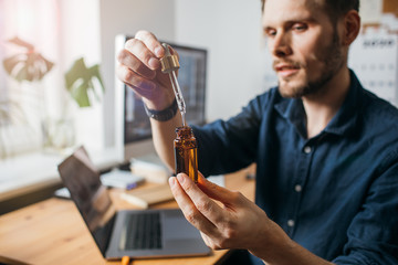Vitamins and supplements. Hand holding pipette of Hemp oil. Close up man uses CBD oil. Medical...