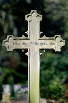 old stone cross with the writing; lord thy will be done, on a grave in a cemetery