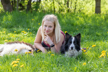 Naklejka na ściany i meble Smiling young blond woman is lying between two Border Collies dogs outdoors and looking at the camera. 